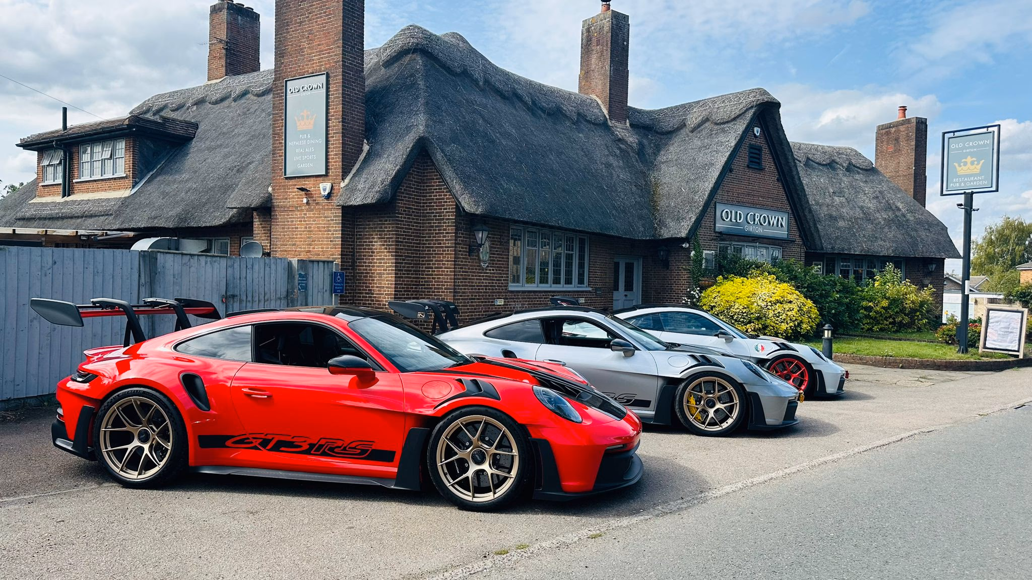 A trio of sports cars parked outside the thatched Old Crown Girton pub on a sunny day